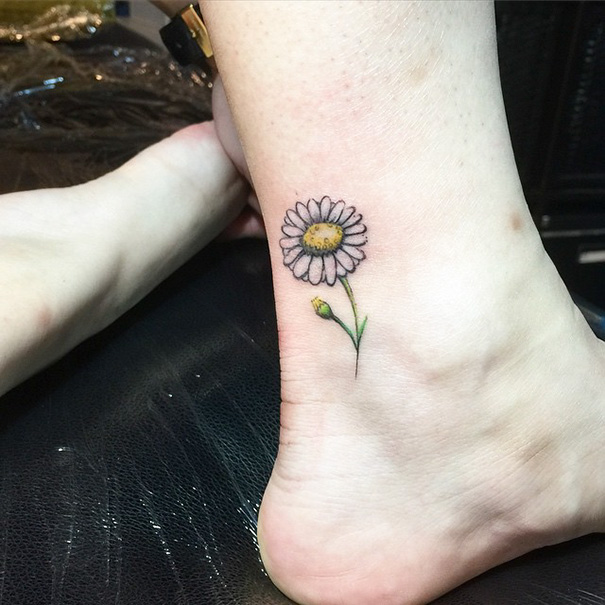 Small foot tattoo of a daisy on ankle, showcasing minimalist design.
