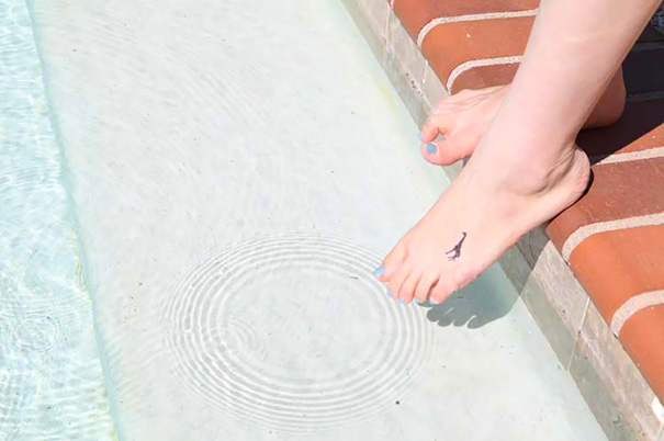 Minimalist small foot tattoo by the pool, showcasing the elegance of less is more design.