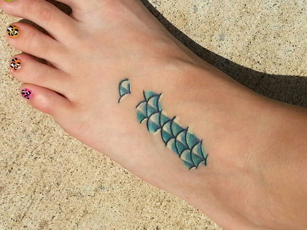 Small foot tattoo featuring blue geometric design, showcasing minimalist art style.