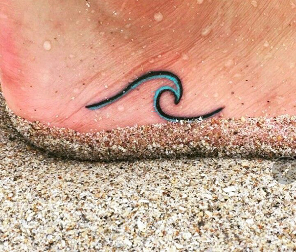 Small wave tattoo on foot with sand, showcasing minimalist foot tattoo ideas.