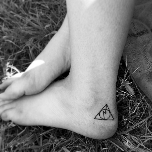 Small foot tattoo of a triangle design, highlighting minimalist tattoo style, on grass background.