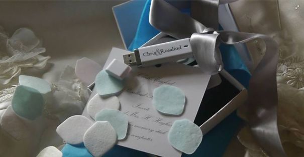 USB wedding invitation in a gift box with ribbon and pastel-colored flower petals for creative wedding invitations.