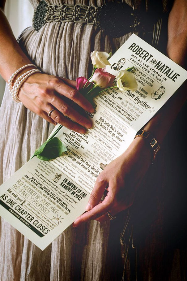 Woman holding creative wedding invitation featuring vintage newspaper design and fresh flowers on elegant dress background