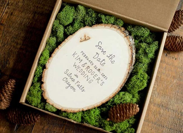 Rustic creative wedding invitation on wood slice with moss and pinecones in a gift box for a unique save the date.
