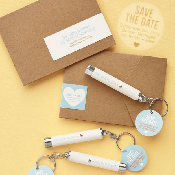 Creative wedding invitations with kraft paper envelopes and unique save the date keychain flashlights on a yellow background.