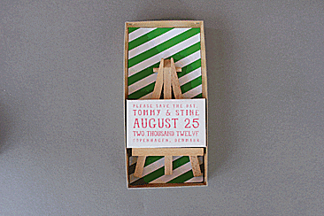 Creative wedding invitation with green and white stripes, personalized text, displayed on a small wooden easel in a box.