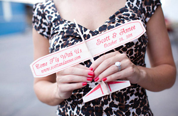 Person holding a creative wedding invitation shaped like an airplane, featuring names and wedding details.