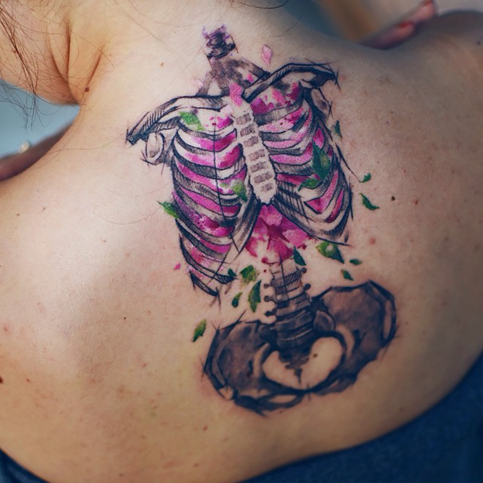 Ethereal nature tattoo of a skeletal ribcage with floral elements, inspired by changing seasons, on a person's back.