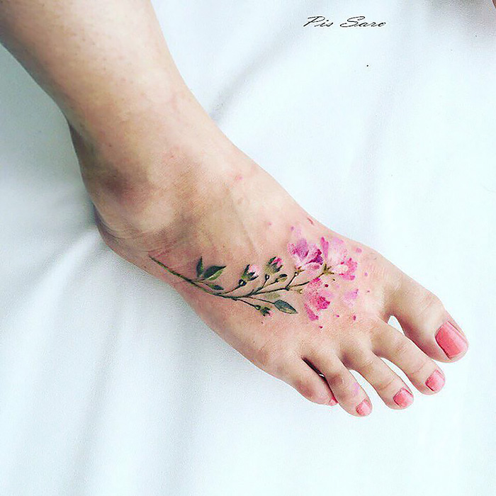 Ethereal nature tattoo of pink blossoms on a foot, inspired by changing seasons.