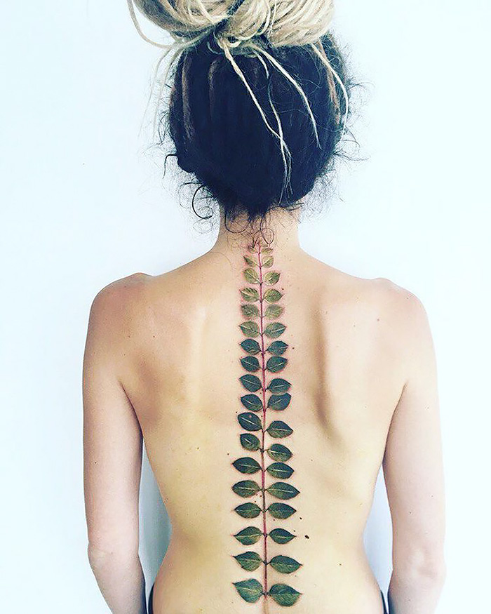 Back view of a person with an ethereal nature tattoo featuring leaves along the spine, symbolizing changing seasons.