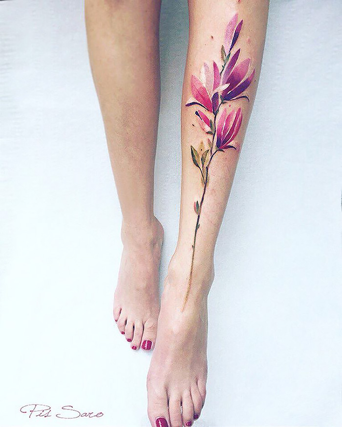 Floral nature tattoo on leg, inspired by changing seasons, featuring pink petals and green leaves.