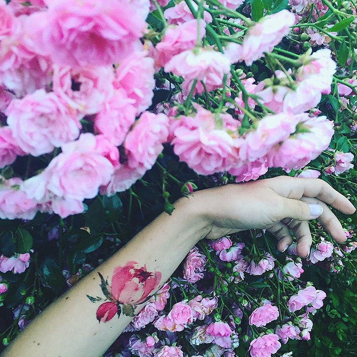 Arm with ethereal nature tattoo amidst vibrant pink blossoms, inspired by changing seasons.