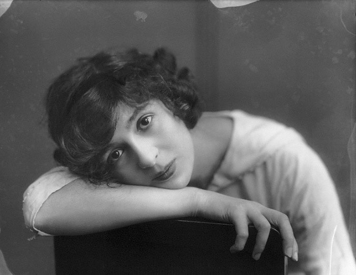 Edwardian era woman with short hair, resting her head on a chair, exuding early 1900s beauty.