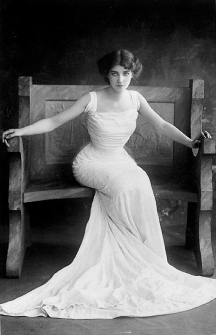 Edwardian era woman in elegant gown seated on a carved wooden bench, showcasing the beauty of early 1900s fashion.