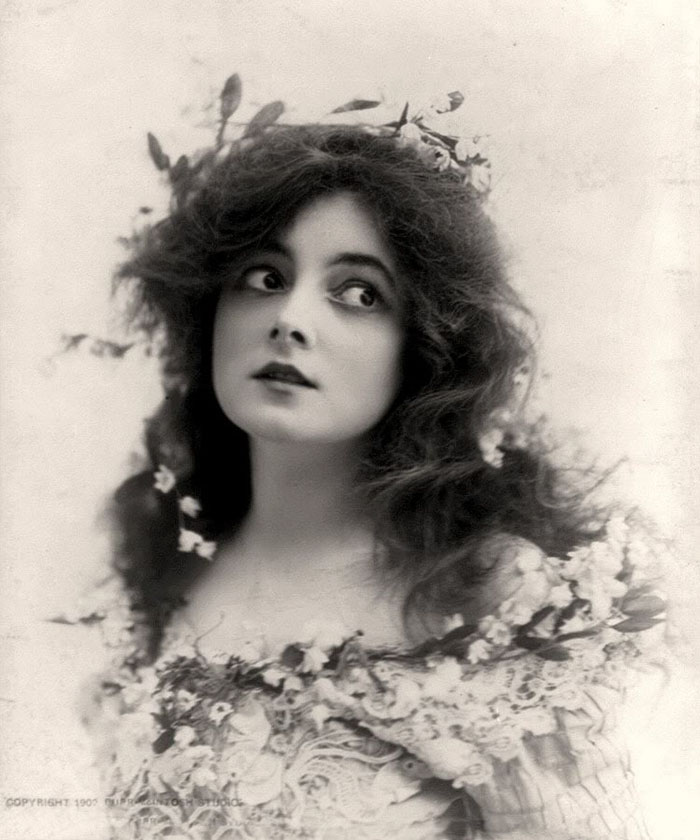 Edwardian era woman with floral dress and headpiece, embodying early 1900s beauty.