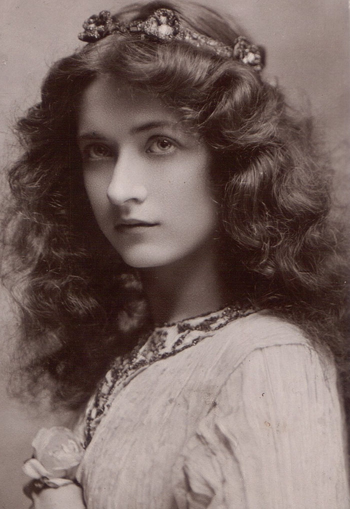 Edwardian era woman with wavy hair and floral headband, gazing softly.