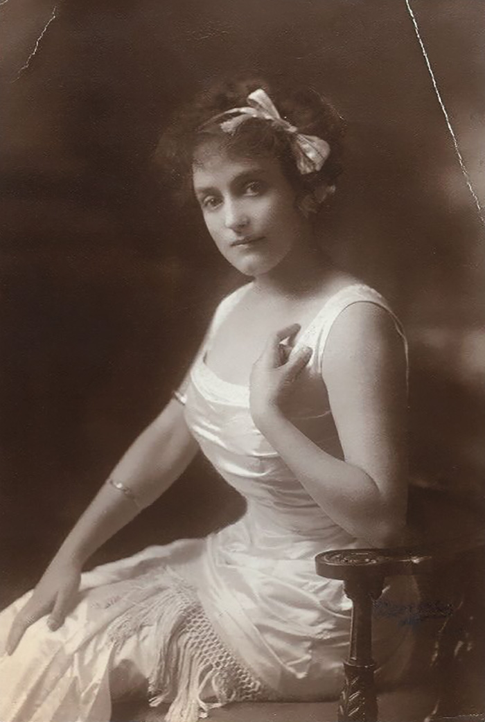 Edwardian era woman seated in a white dress with a bow in her hair, embodying early 1900s beauty style.