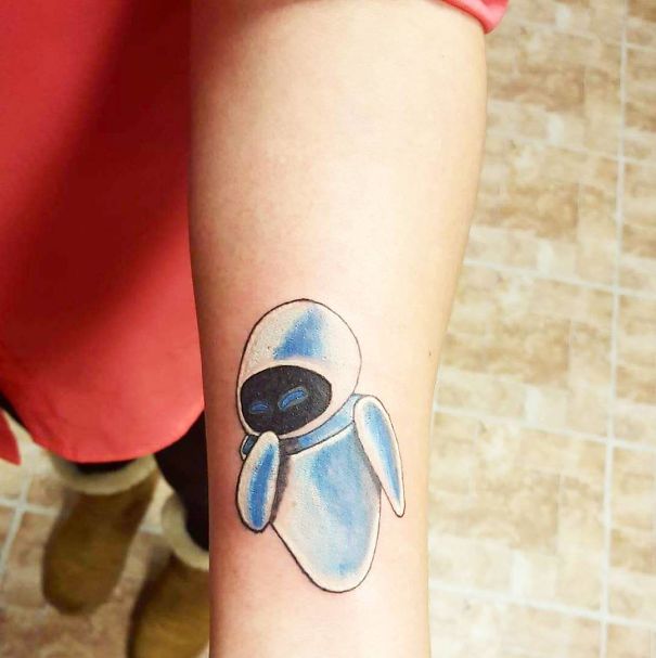 Pixar-inspired tattoo of a blue and white robot on a forearm, showcasing creative design.
