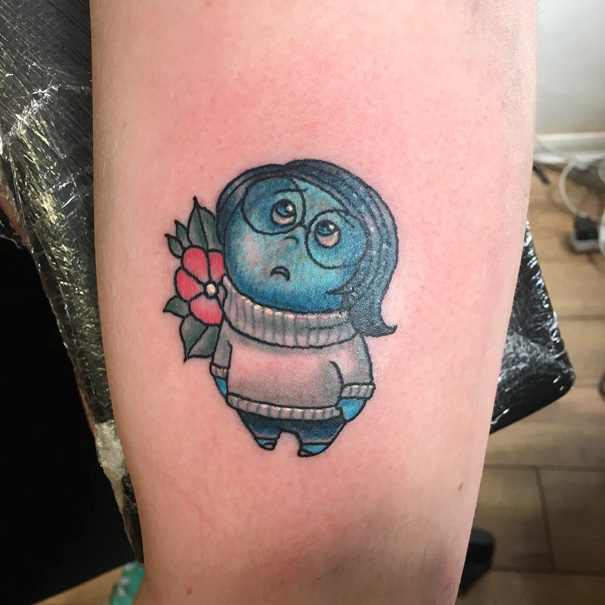 Pixar-inspired tattoo of a blue character holding a pink flower, designed on an arm.
