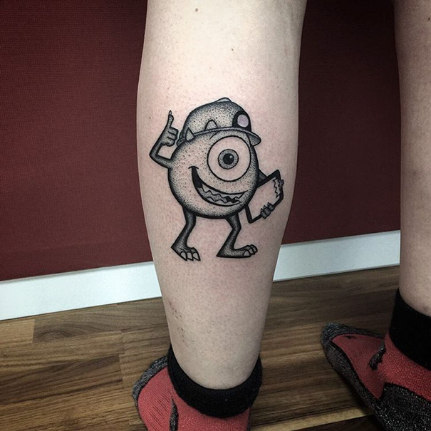 Pixar-inspired tattoo of a smiling, one-eyed character on a person's calf with a hat and pointing gesture.