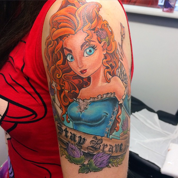 Pixar-inspired tattoo featuring a red-haired character with "Stay Brave" banner on a person's upper arm.