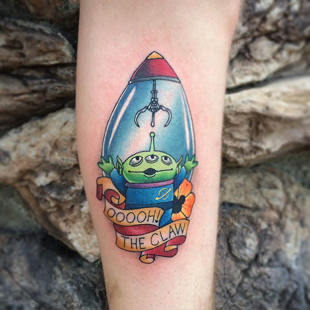 Pixar-inspired tattoo of a green alien under a claw machine, with a banner reading "OOooh! The Claw."