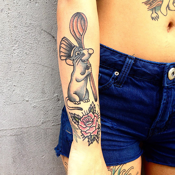 Pixar-inspired tattoo of a cartoon rat holding a whisk, with a rose design on the forearm.