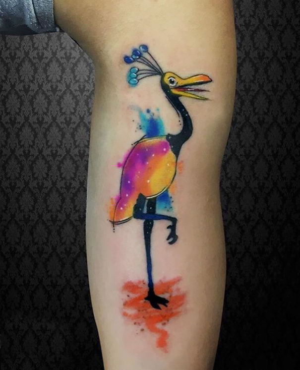 Colorful Pixar-inspired bird tattoo on forearm with vibrant hues and abstract background.