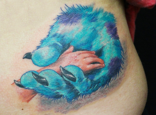 Pixar-inspired tattoo of a blue furry paw clutching a small hand, showcasing vibrant colors and detailed art.
