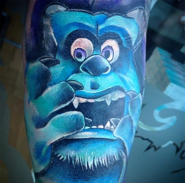 Pixar-inspired tattoo featuring a detailed blue monster with expressive eyes and hands.