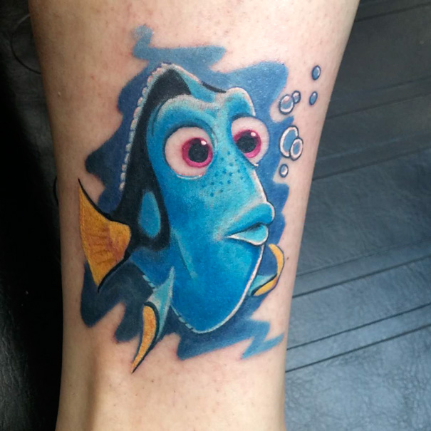 Pixar-inspired tattoo of a blue fish character with yellow fins and bubbles on skin.