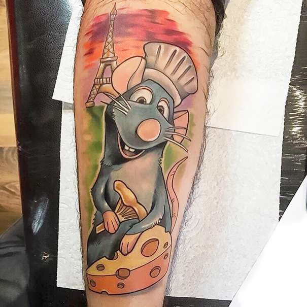 Pixar-inspired tattoo featuring a cartoon rat chef with Eiffel Tower and cheese, on a person's leg.