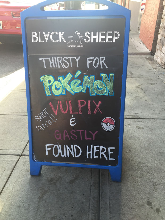 Chalkboard sign promoting Pokémon drink specials featuring Vulpix and Gastly at Black Sheep burgers and shakes.