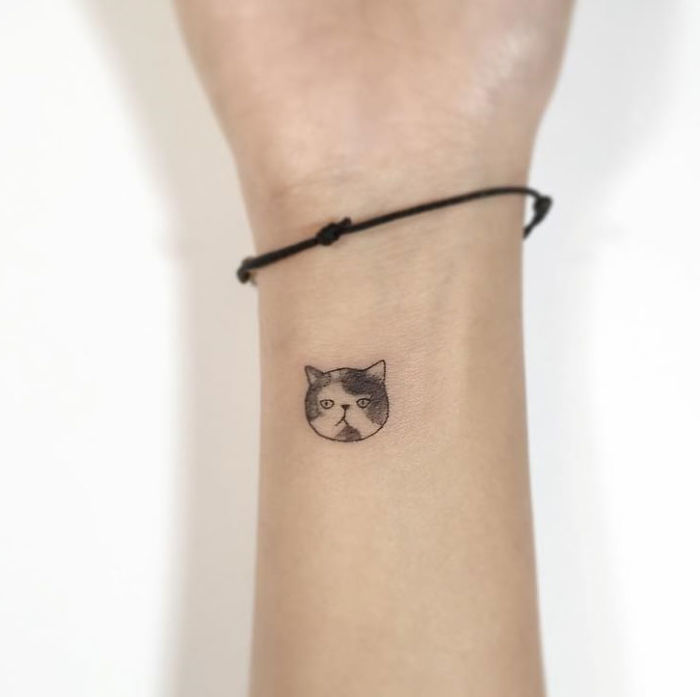 Minimalist tattoo of a cat's face on a wrist by a Korean artist.