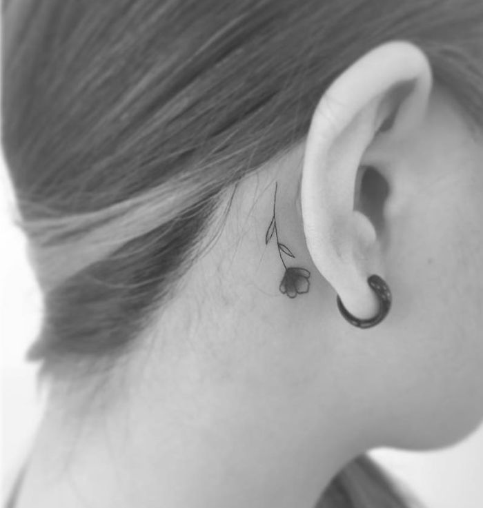 Minimalist tattoo of a flower behind the ear, created by a Korean artist.