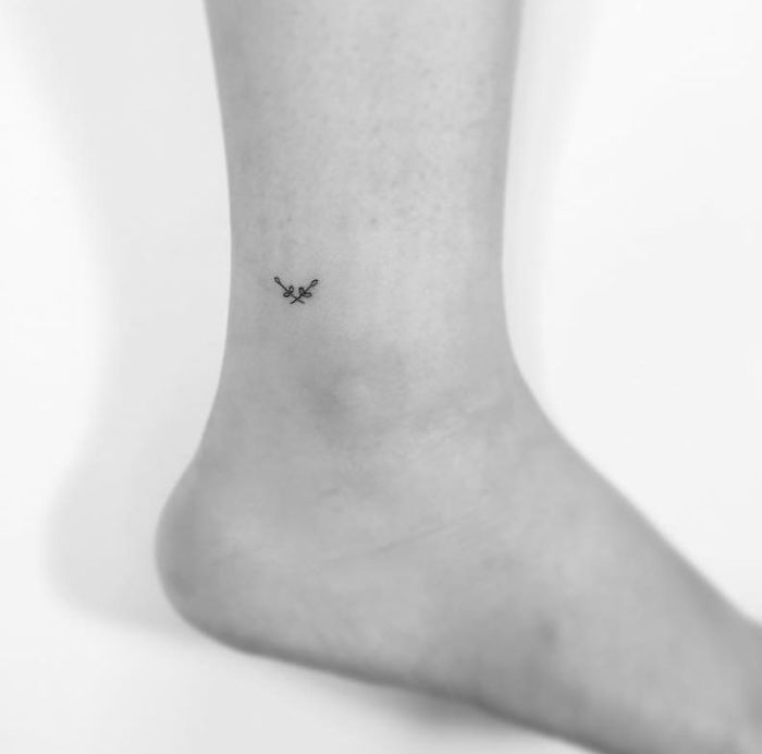 Minimalist tattoo of small branches on an ankle, created by a Korean artist.