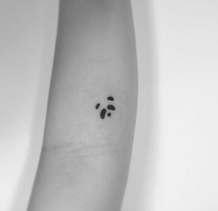 Minimalist tattoo by Korean artist on forearm, featuring small abstract black shapes on smooth skin.