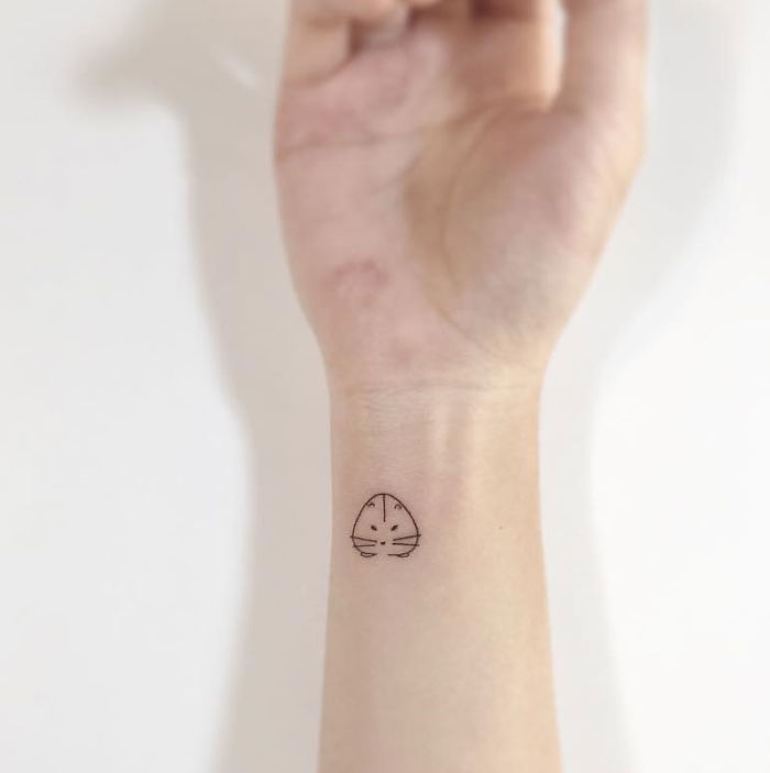 Minimalist Korean tattoo of a simple cat face on a wrist.