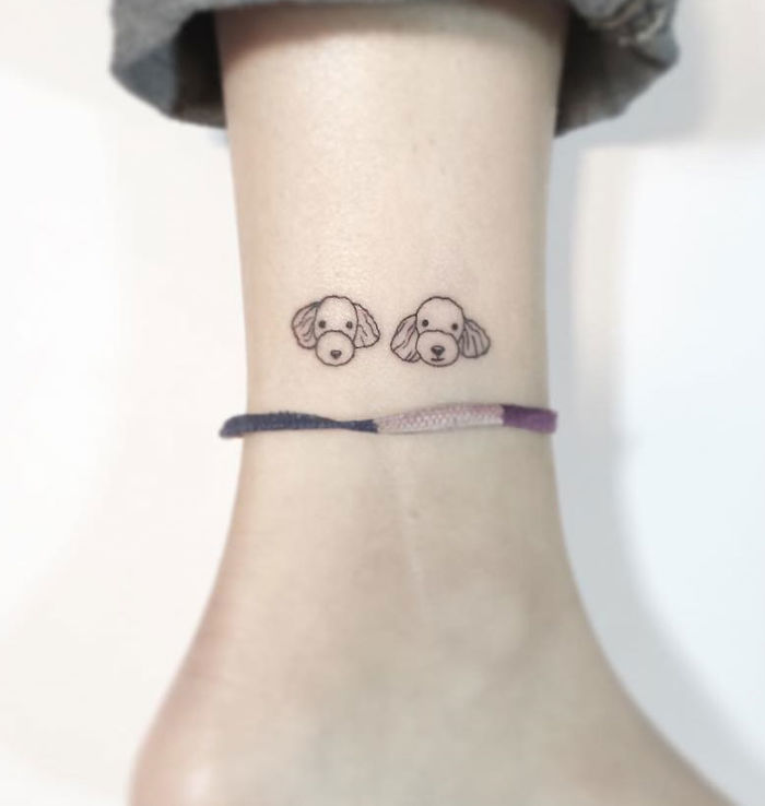 Minimalist tattoo of two dog faces on an ankle by a Korean artist, featuring a simple line design.