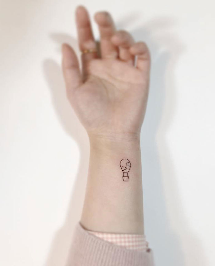 Minimalist tattoo of a small light bulb on a person's wrist, created by a Korean artist.