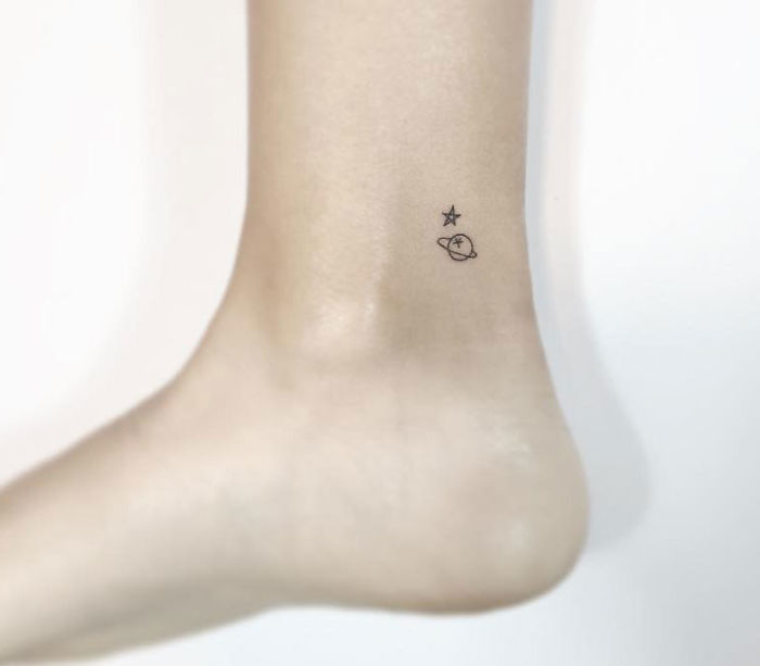 Minimalist tattoo of a star and planet on an ankle by a Korean artist.