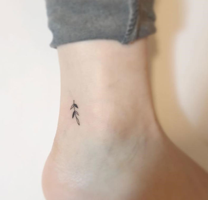 Minimalist tattoo featuring delicate leaf design on ankle by Korean artist.