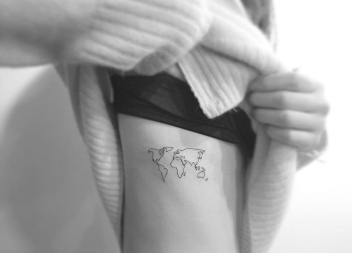 Minimalist tattoo of a world map on a person's side, designed by a Korean artist.