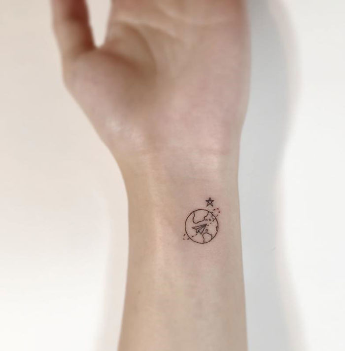 Minimalist tattoo of a small plane and star on a wrist, designed by a Korean artist.