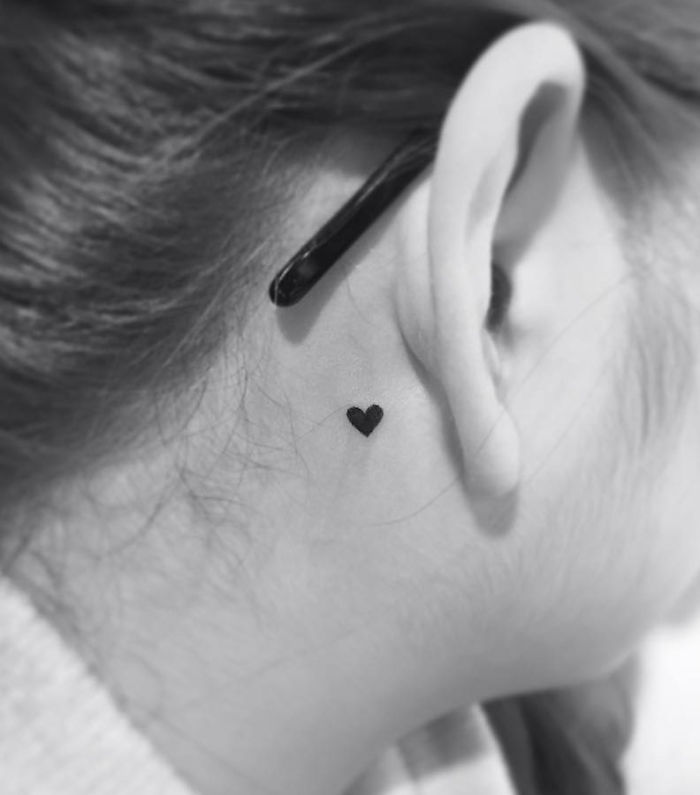 Minimalist heart tattoo behind ear by a Korean artist, showcasing simple and elegant design.