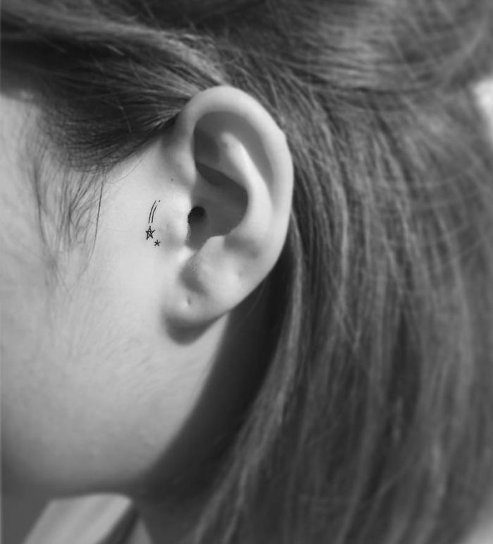 Minimalist tattoo of small stars inside an ear, showcasing Korean artistry.