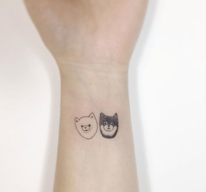 Minimalist tattoos of two cute animal faces on a person's wrist by a Korean artist.