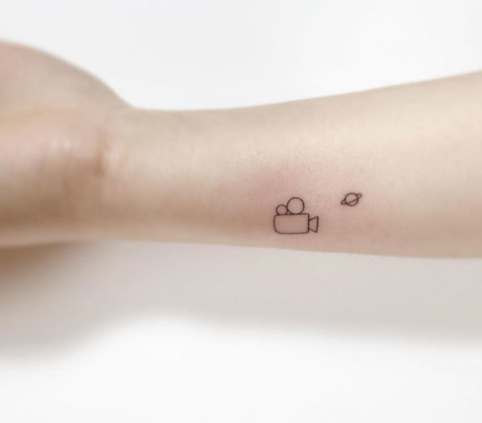 Minimalist tattoos of a camera and planet inked on forearm by Korean artist.