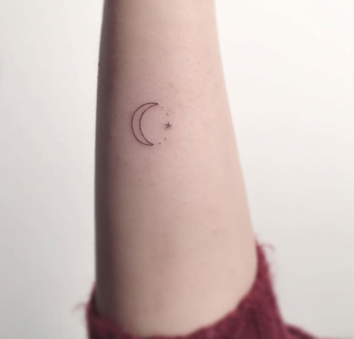 Minimalist tattoo of a crescent moon and star on an arm, created by a Korean artist.