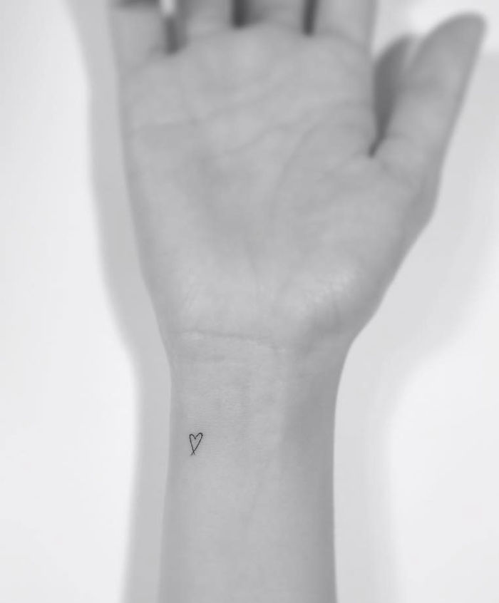 Minimalist tattoo of a small heart on a person's wrist, designed by a Korean artist.
